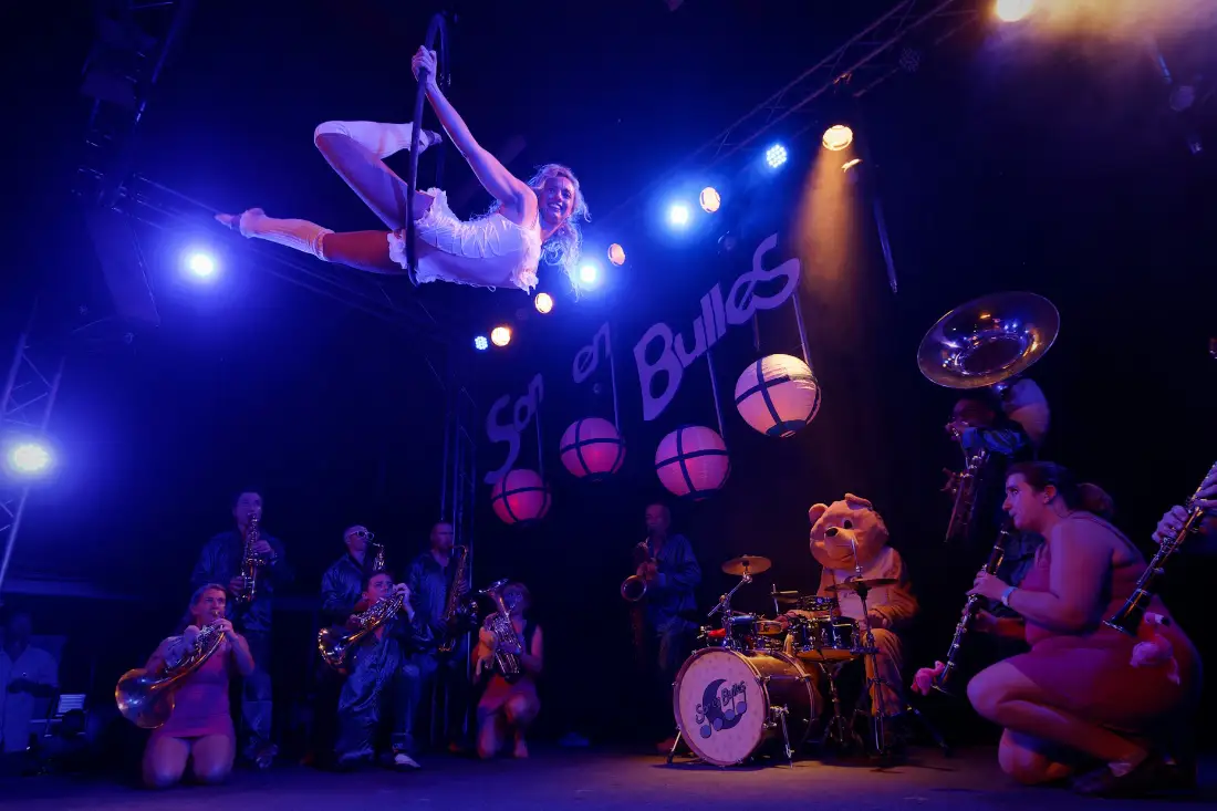 Acrobat flying high above a band on a lit stage